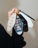 Hand holding assorted motel-style keychains including the Hot Girls Hit Curbs Keychain