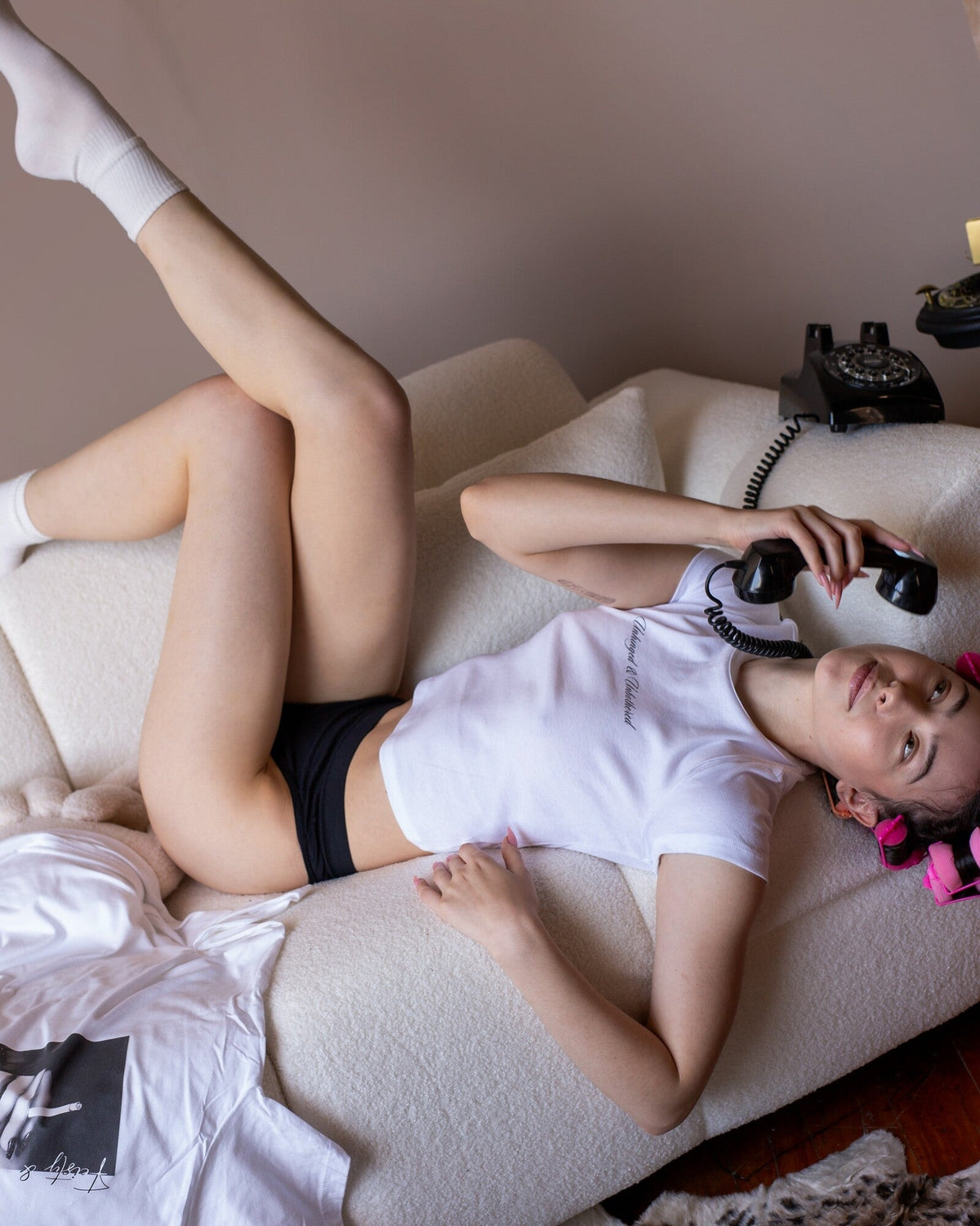 Model wearing the white Unhinged & Unbothered baby tee in a bedroom lifestyle photo.