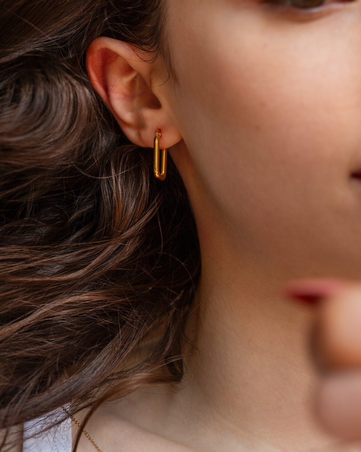 Circe elongated rectangular gold hoop styled in a side portrait.