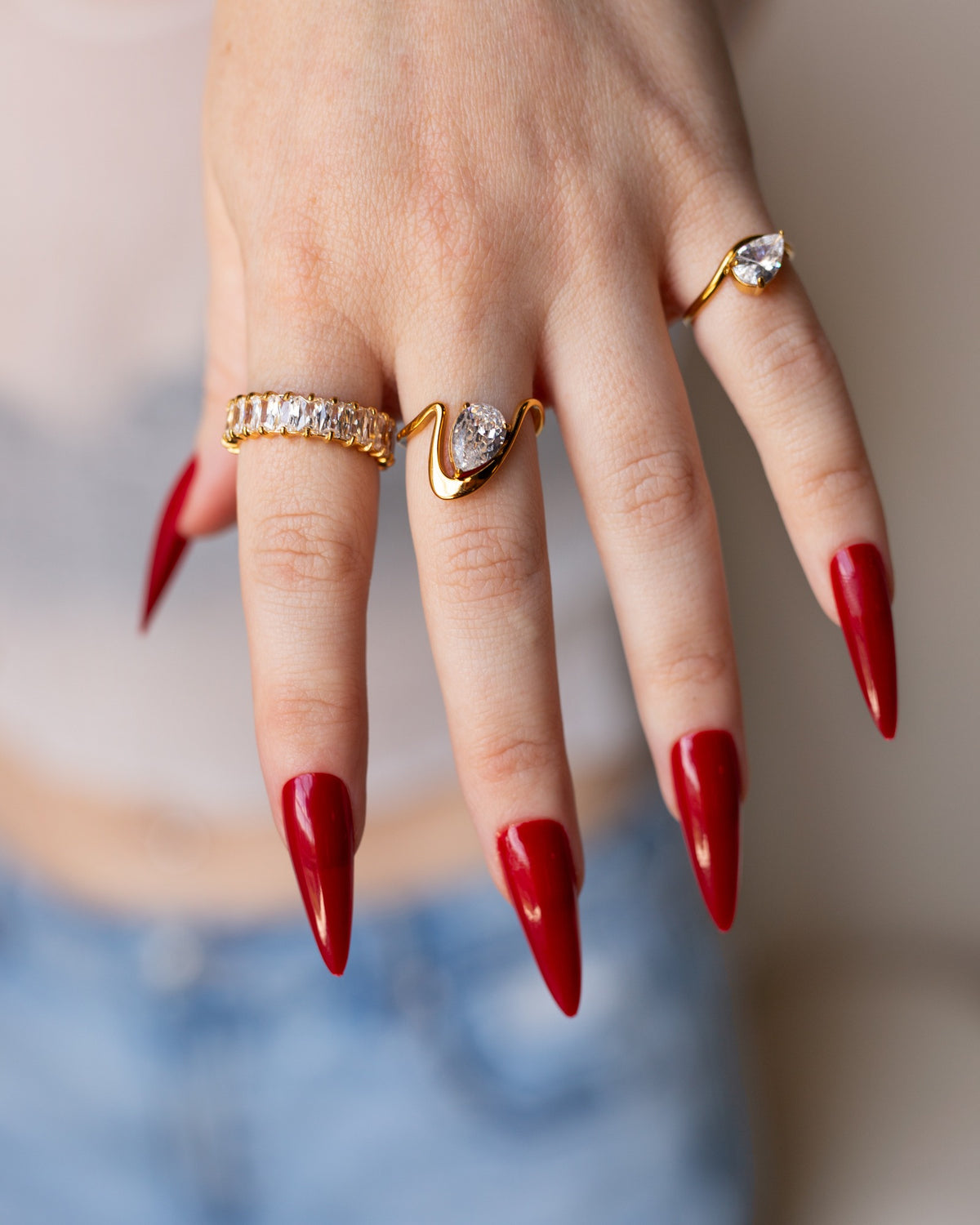 Davina horizontal pear-stone ring styled with layered gold rings and long red nails in a hand portrait.