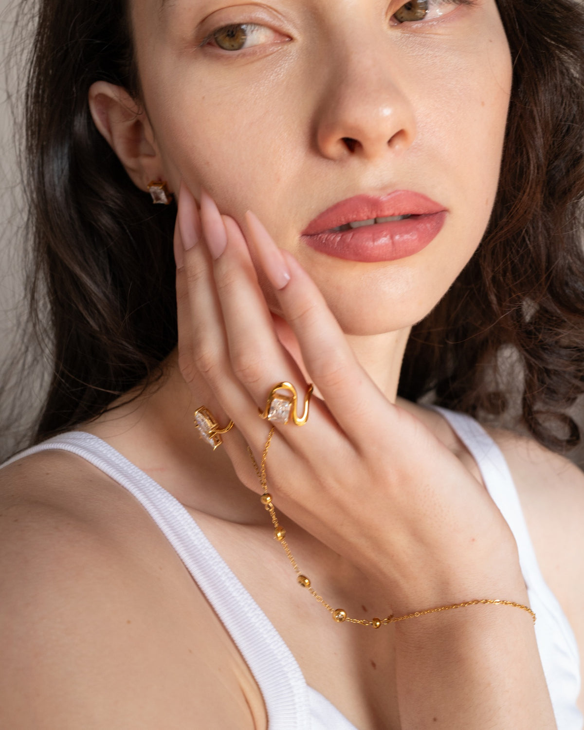 Diana square-stone wave ring worn with pale pink nails in a close hand-to-face portrait.
