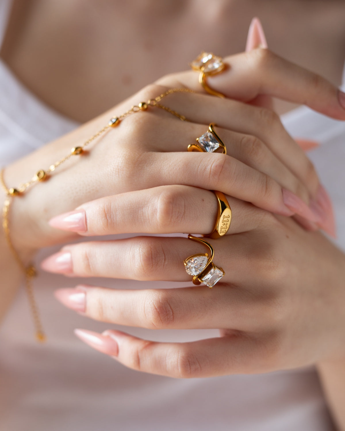 Diana princess-cut wave ring styled with layered gold rings and pale pink nails in a close hands detail.