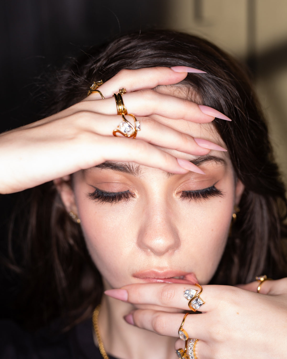 Diana sculptural gold ring worn with clear-stone rings in a hands-framing-face portrait.