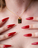 Close-up of a model wearing the gold Fuck Off Necklace with red nails framing the pendant.