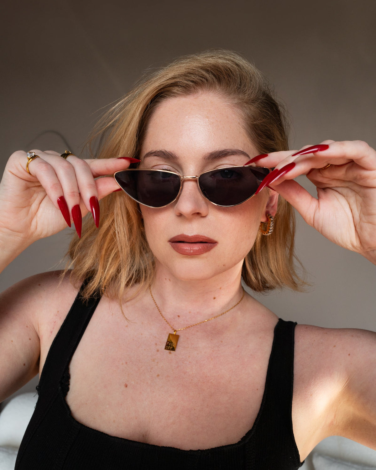 Model wearing the gold Fuck Off Necklace with black sunglasses and red nails.