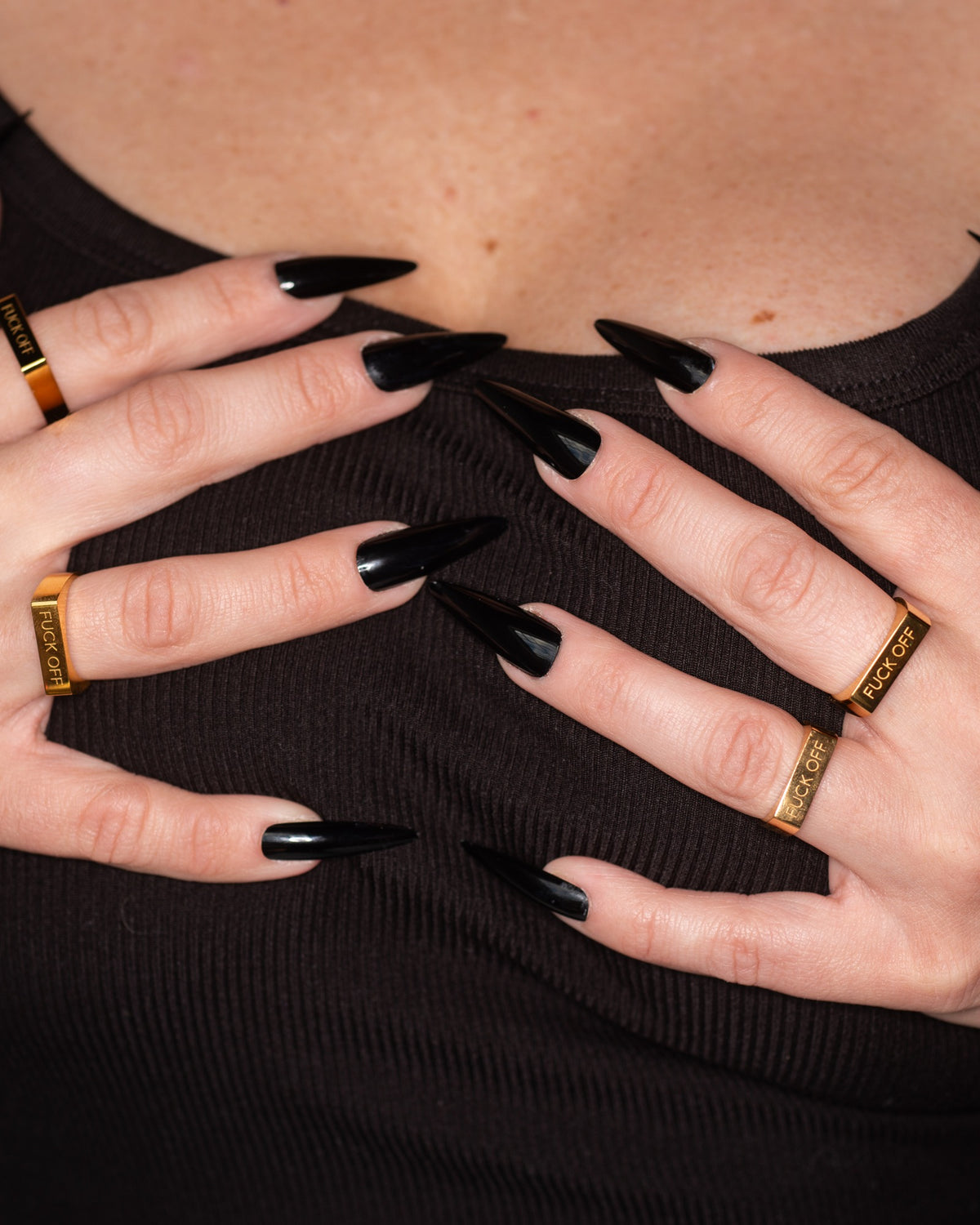 Fuck Off engraved ring worn with multiple gold rings and black nails.