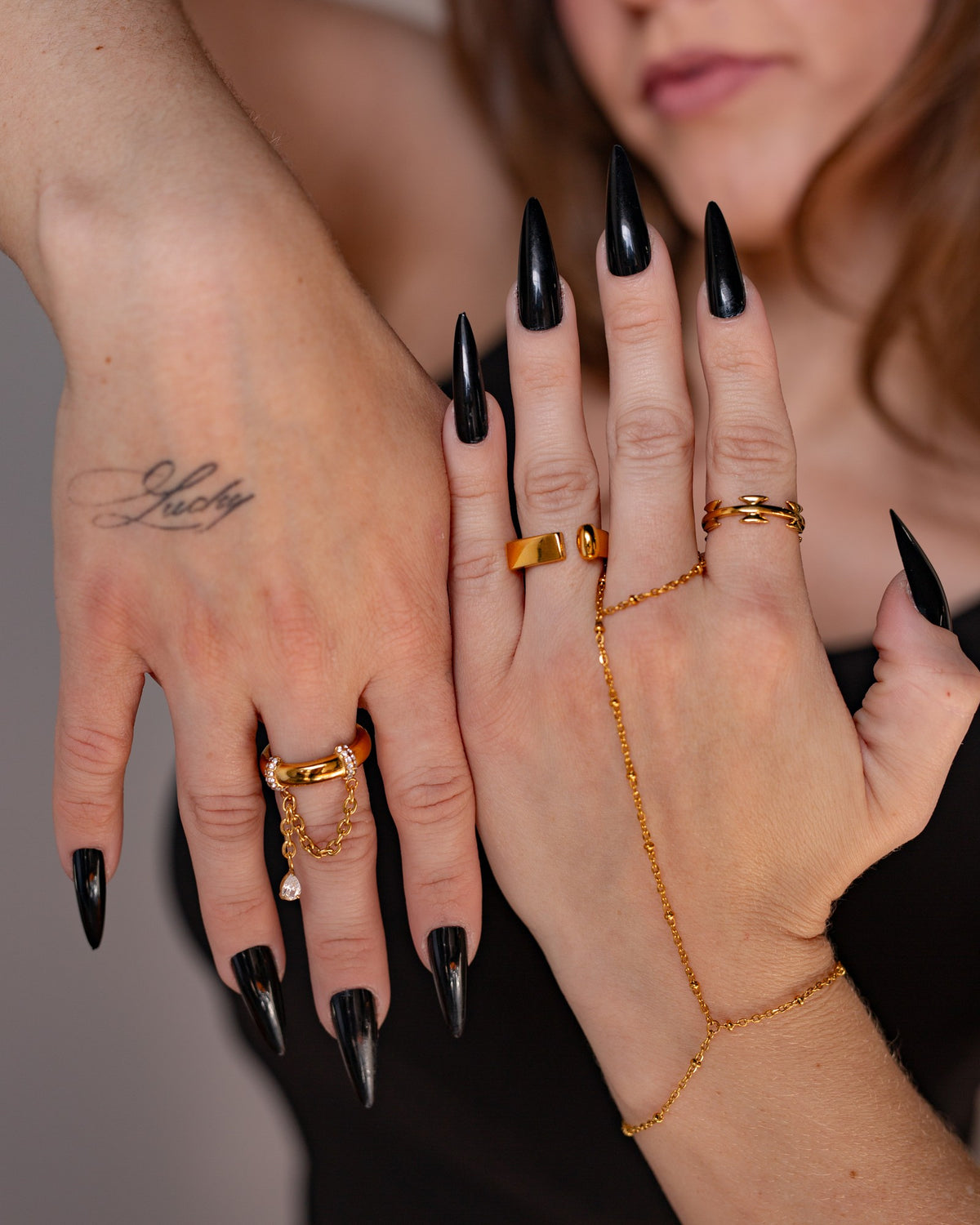Gina gold chain statement ring styled with layered hand jewelry and black nails.