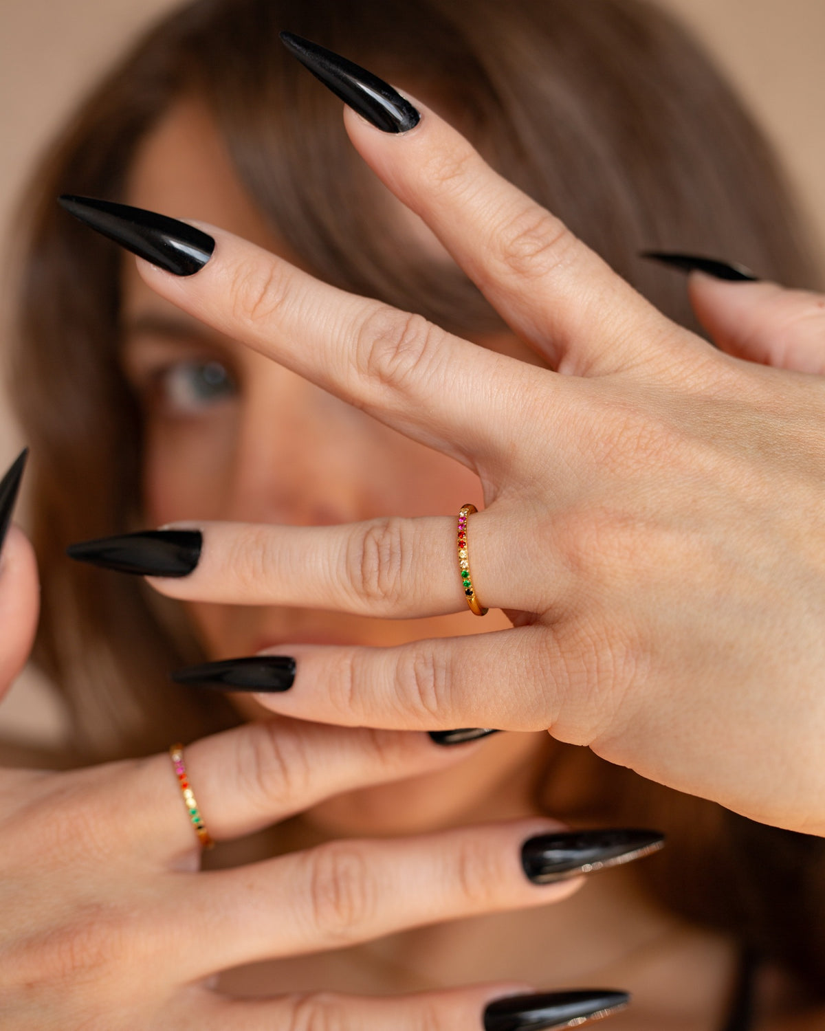 Iris rainbow pavé stacking ring worn on both hands with long black nails in a close portrait.