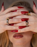 Lin mixed-metal knot ring worn with red nails in a tight hands-across-face detail.