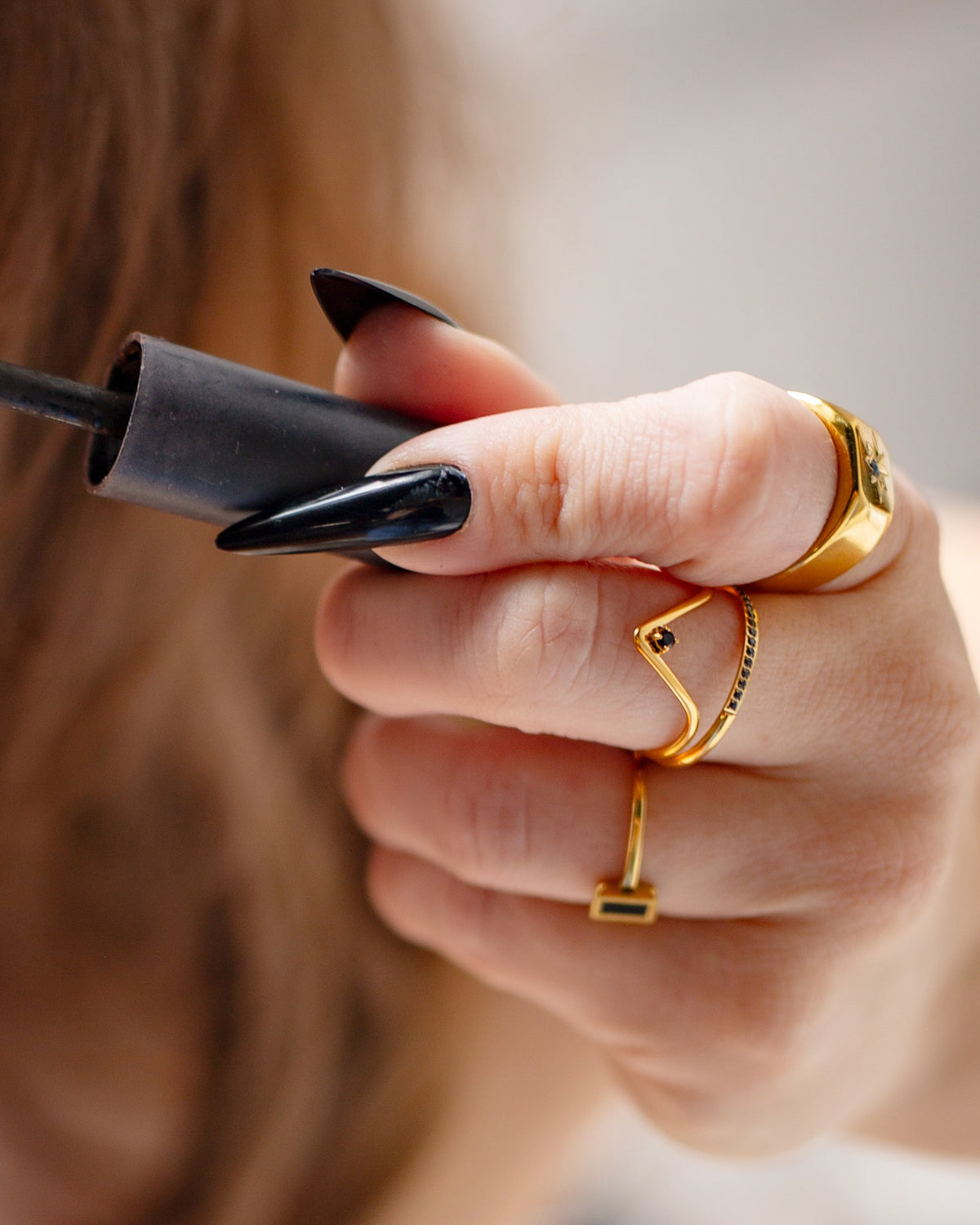 Manto black pear-stone wave ring worn with long black nails while holding a mascara wand.