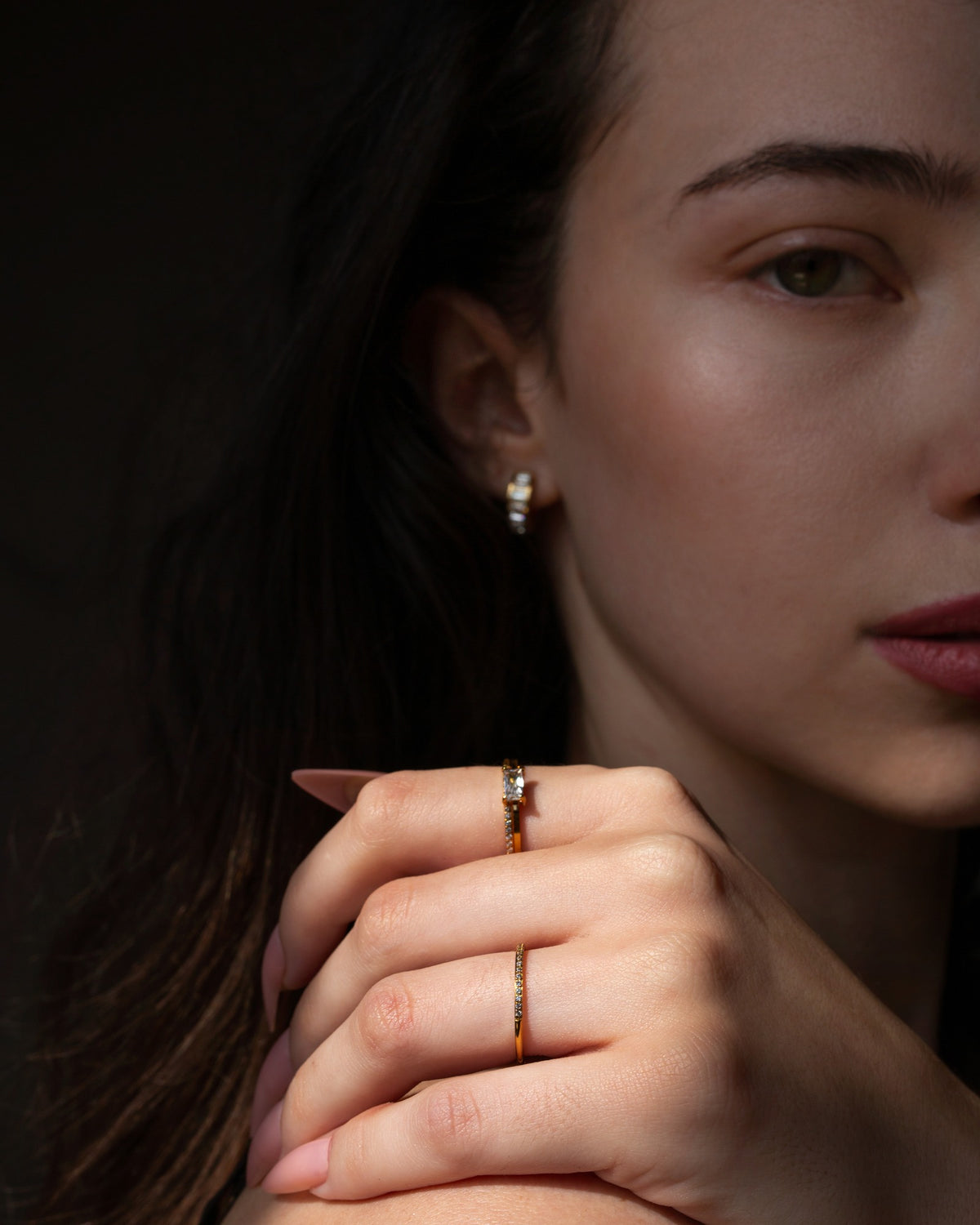 Nelle rectangular clear-stone ring styled in a dark close portrait with pale pink nails.
