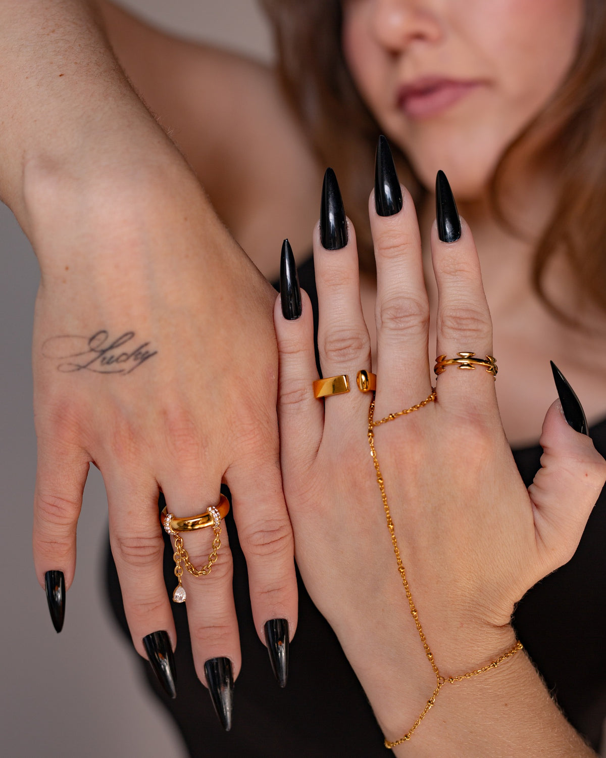 Nemesis angular cutout ring worn with a delicate gold hand chain and long black nails in a close two-hand detail.