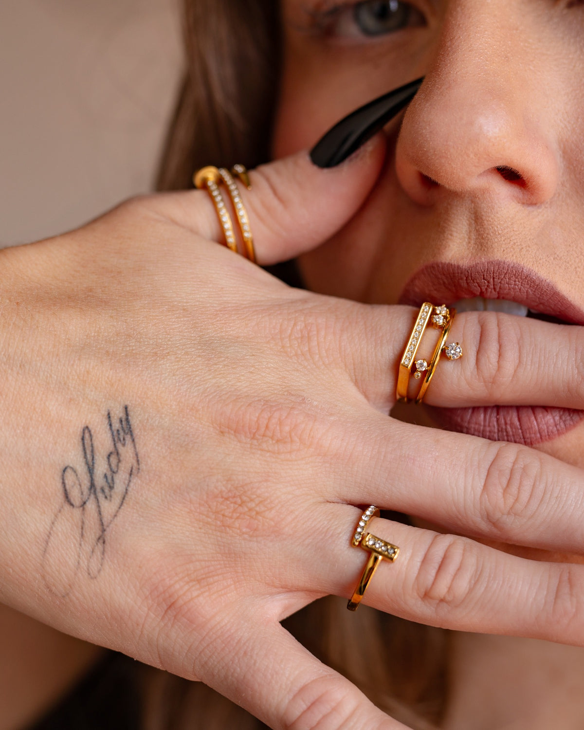 Noor clear-stone bypass ring worn with black nails in a tight hand-to-face detail.