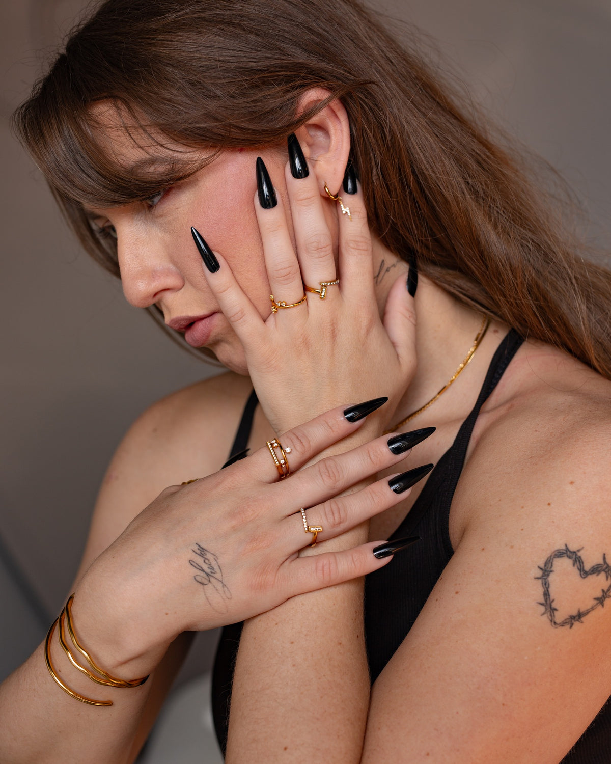 Noor gold clear-stone ring styled in a portrait with layered jewelry and black nails.