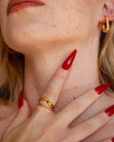 Nysa twisted rope gold ring worn with layered bands and long red nails in a close neck portrait.