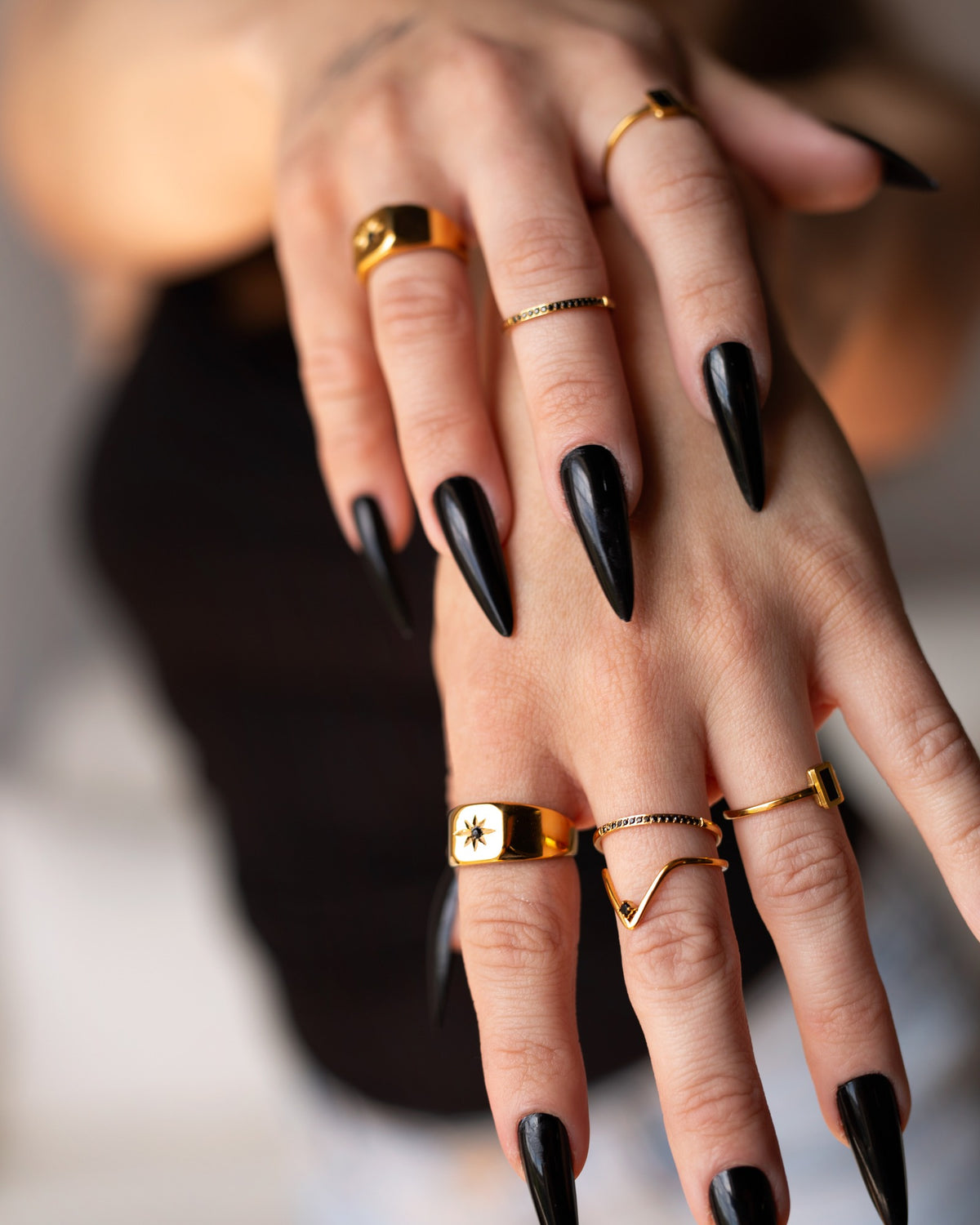 Nyx black-stone stacking ring styled with bold gold rings and long black nails.