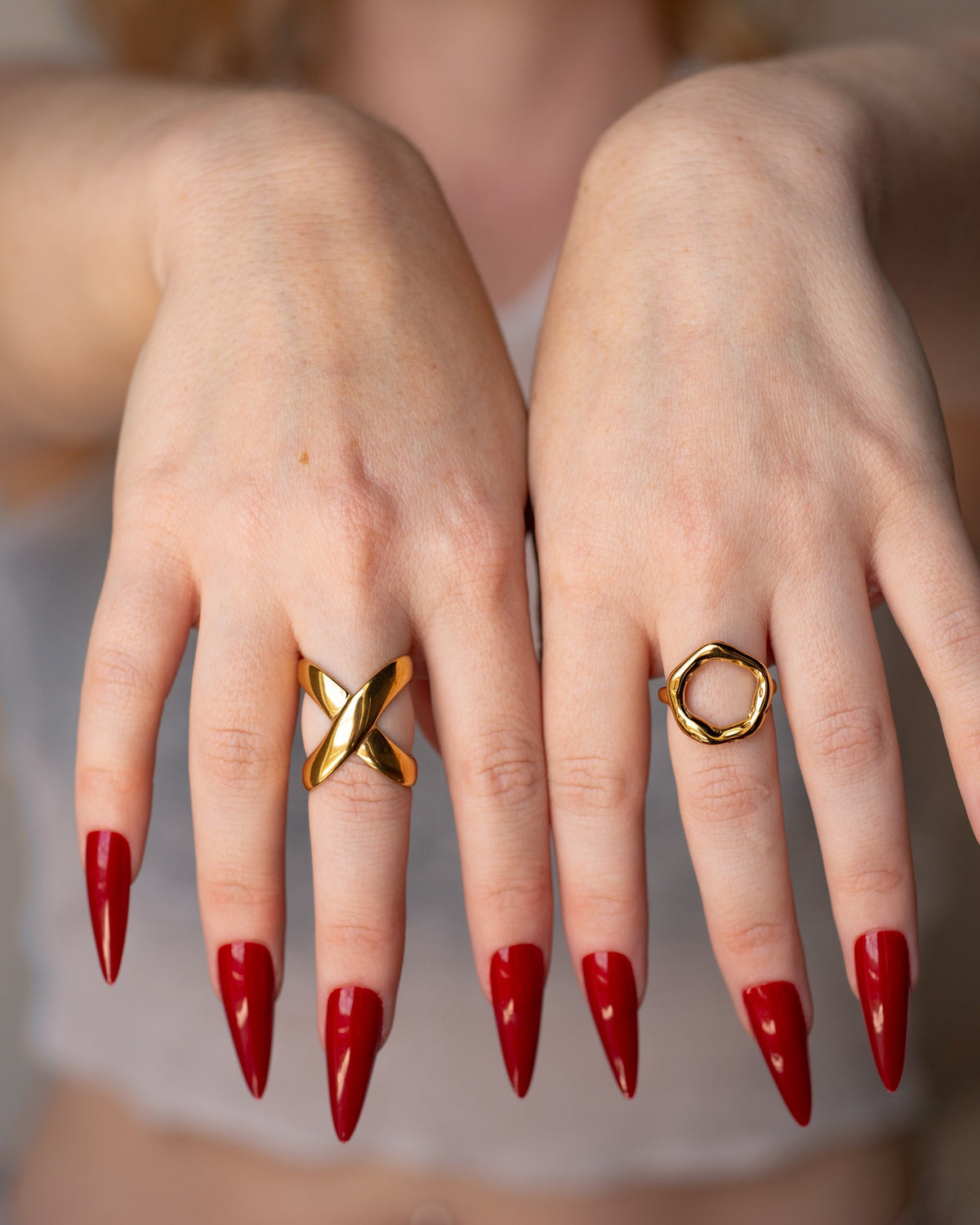 O Ring worn on hand beside a sculptural gold statement ring with red nails.