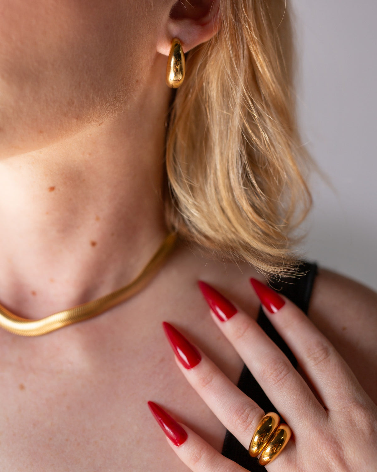 Octavia chunky gold band worn with long red nails in a close hand-to-neck portrait.