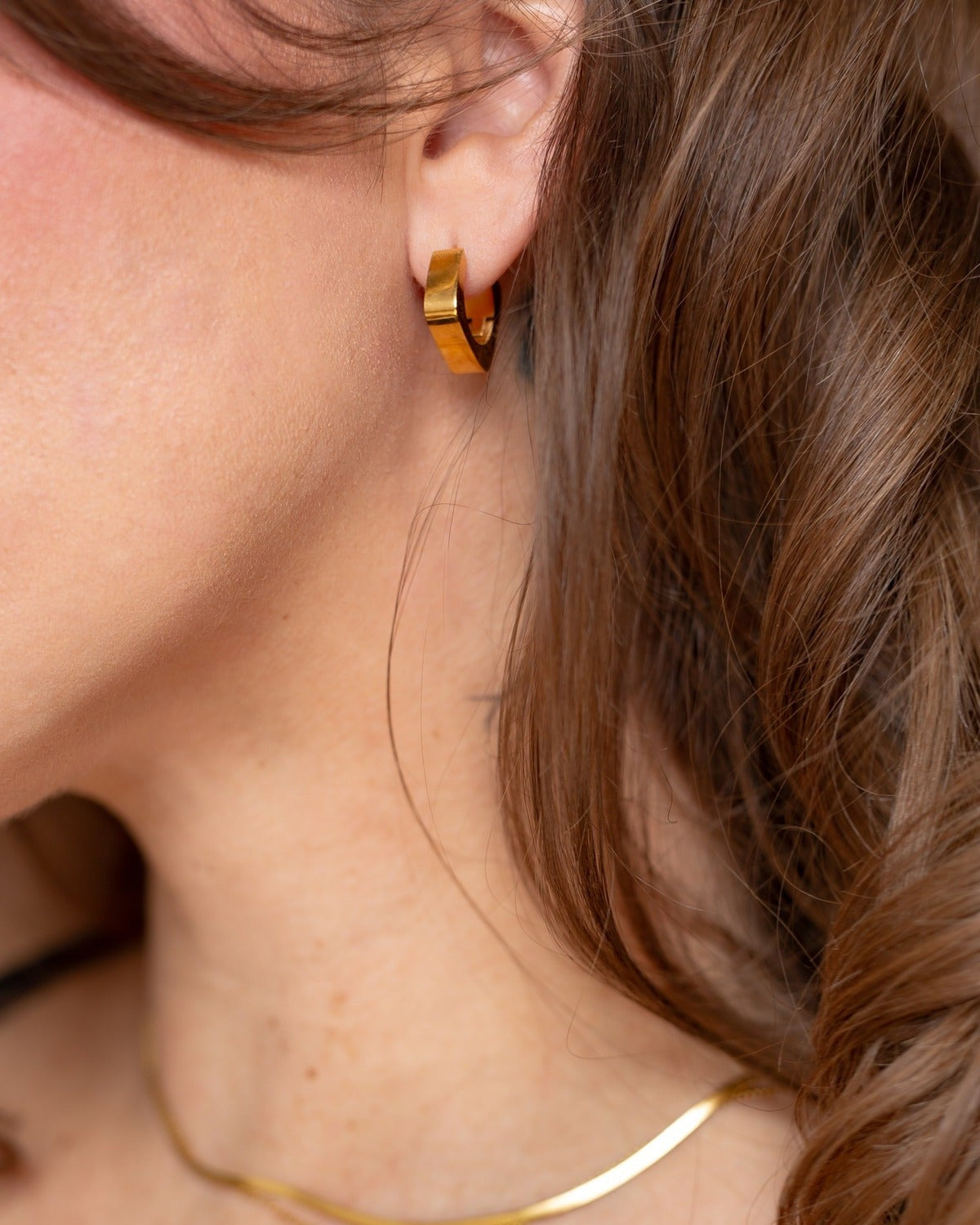 Rhea rounded square gold hoop worn in a close-up portrait.