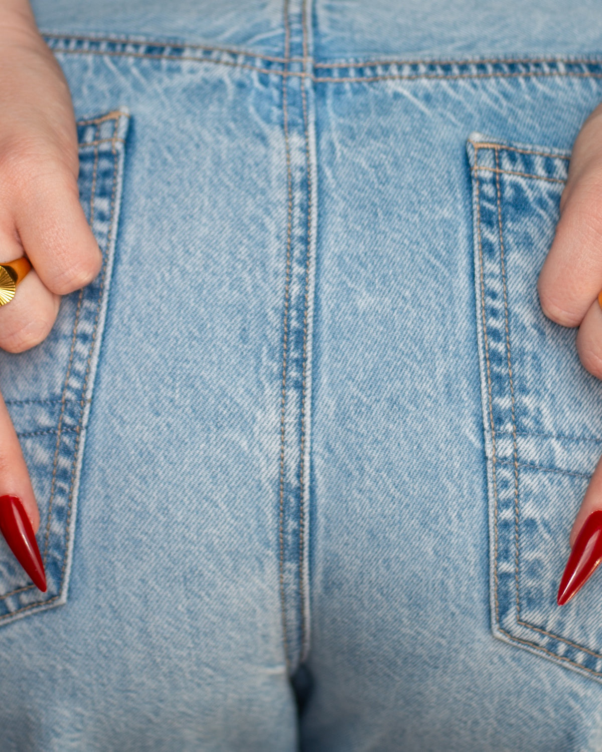 Sol gold sunburst signet ring styled on both hands with long red nails and blue denim.