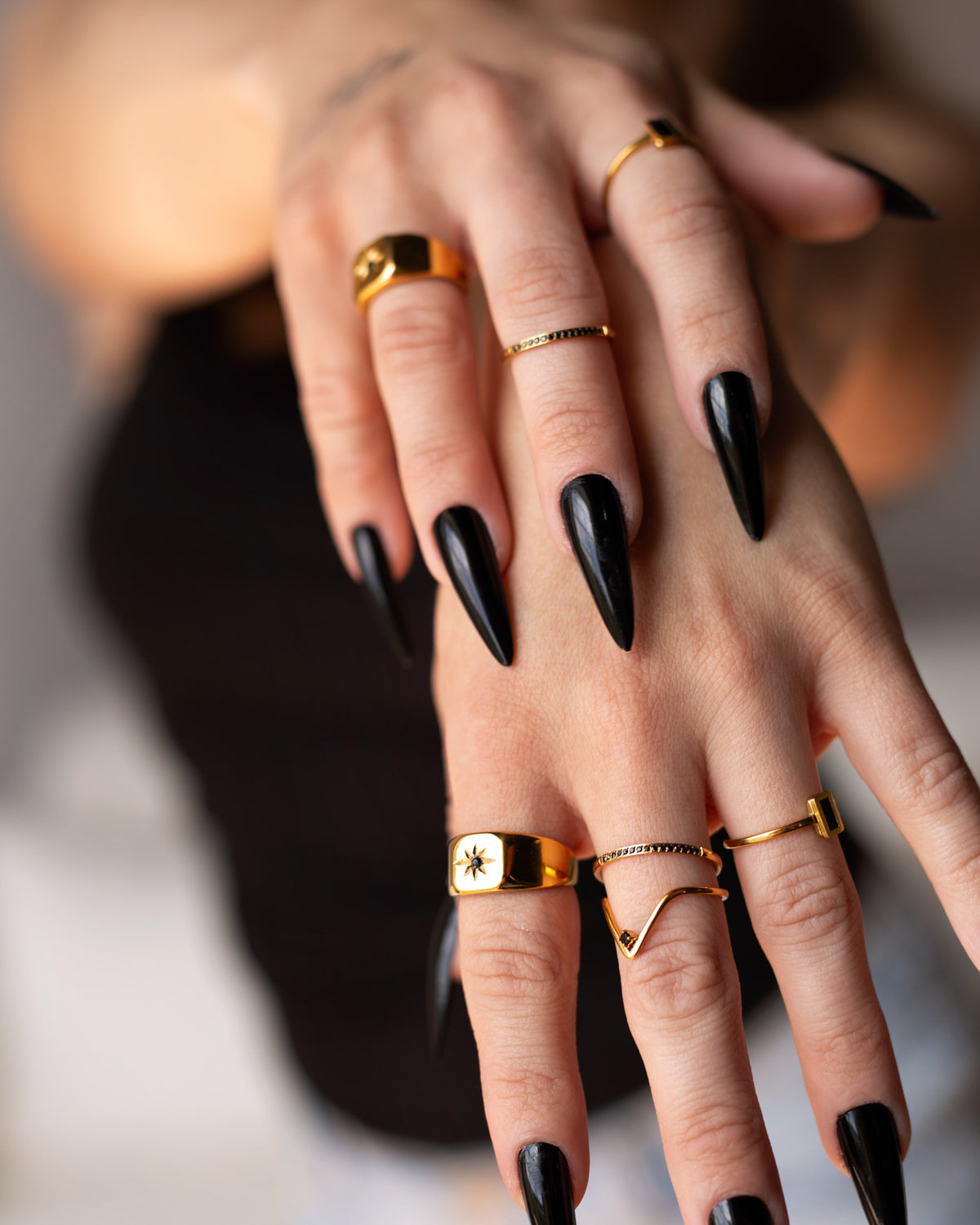 Summer gold signet ring styled with layered rings and long black nails in a two-hand detail.