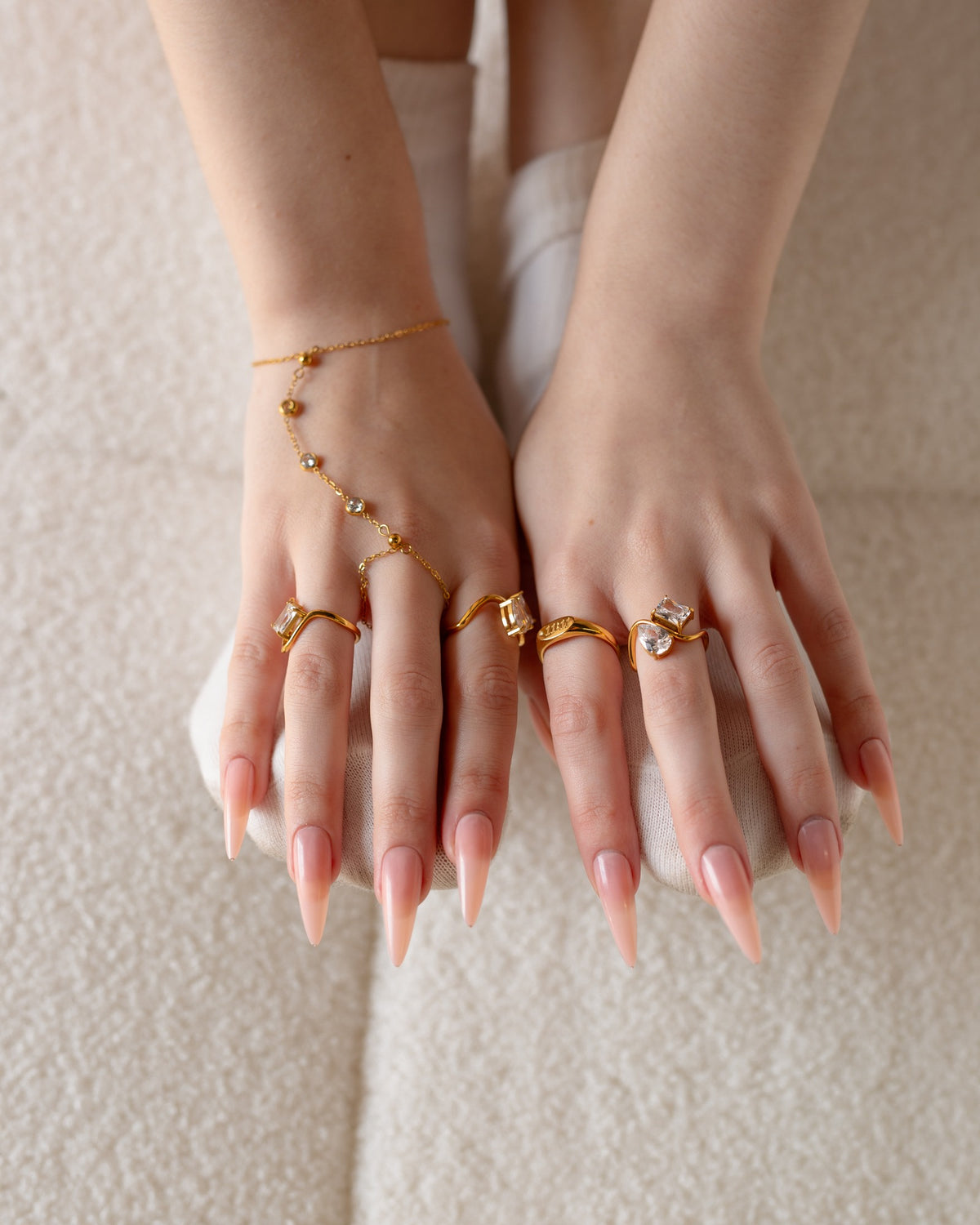 Talia gold two-stone ring shown with both hands and layered gold rings in a seated detail.